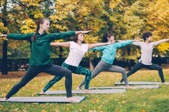 Yoga class is doing stretching exercises in park enjoying autumn nature, fresh air and physical activity. Well-being, recreation and sporty young people concept.